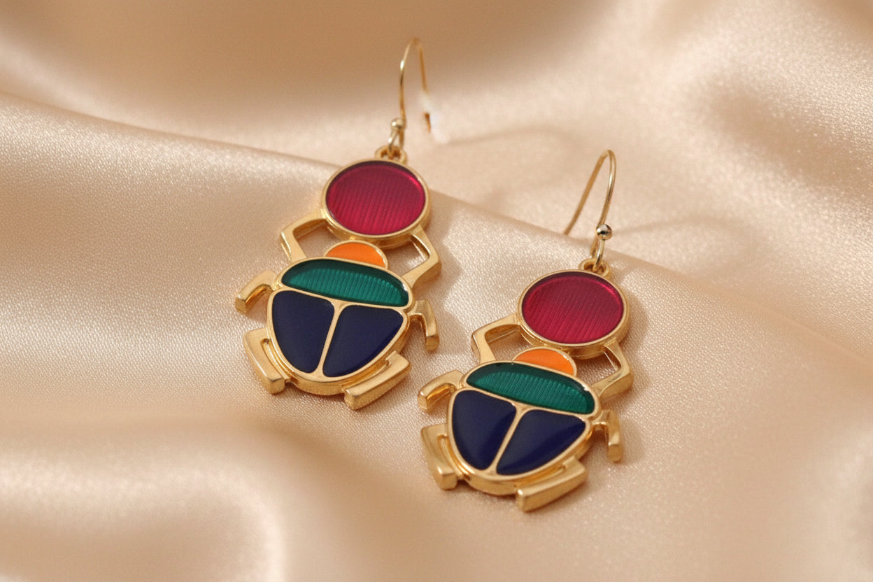 Boucles d’oreilles Kheper dorées avec détails colorés, présentées seules sur fond soyeux