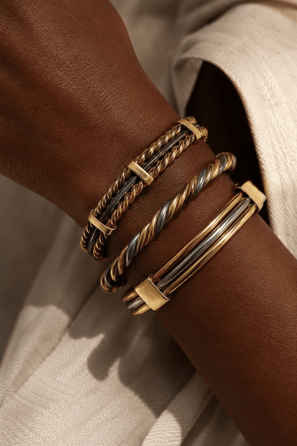 Triptyque Lamou Ndiaxass : les trois bracelets portés ensemble au poignet, sur une tenue crème