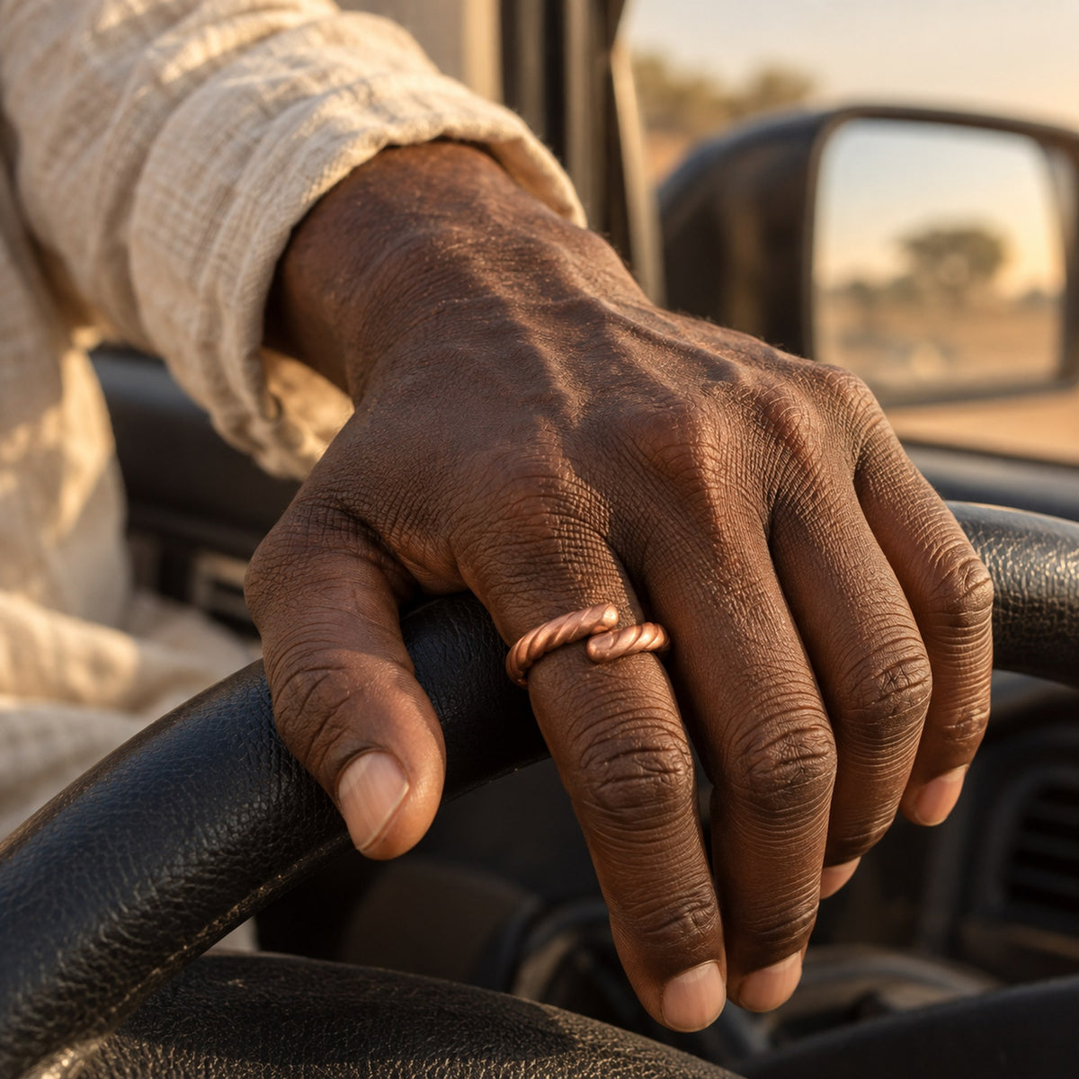 Main d'homme portant la bague Djigui en cuivre, posée sur un volant