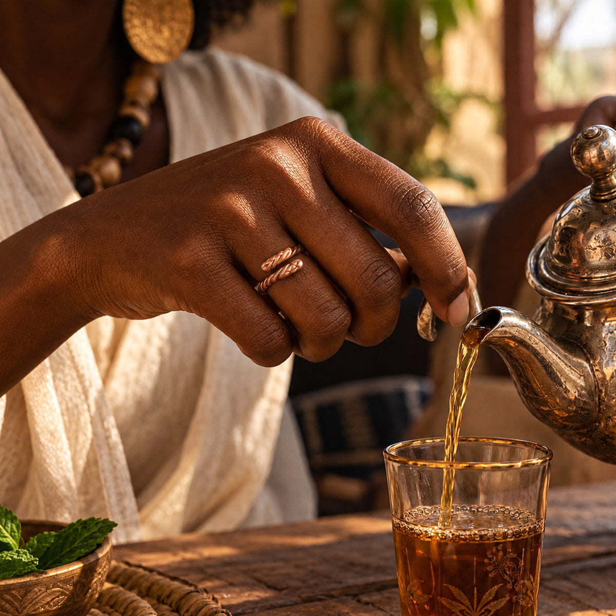 Main de femme portant la bague Djigui en cuivre en servant le thé