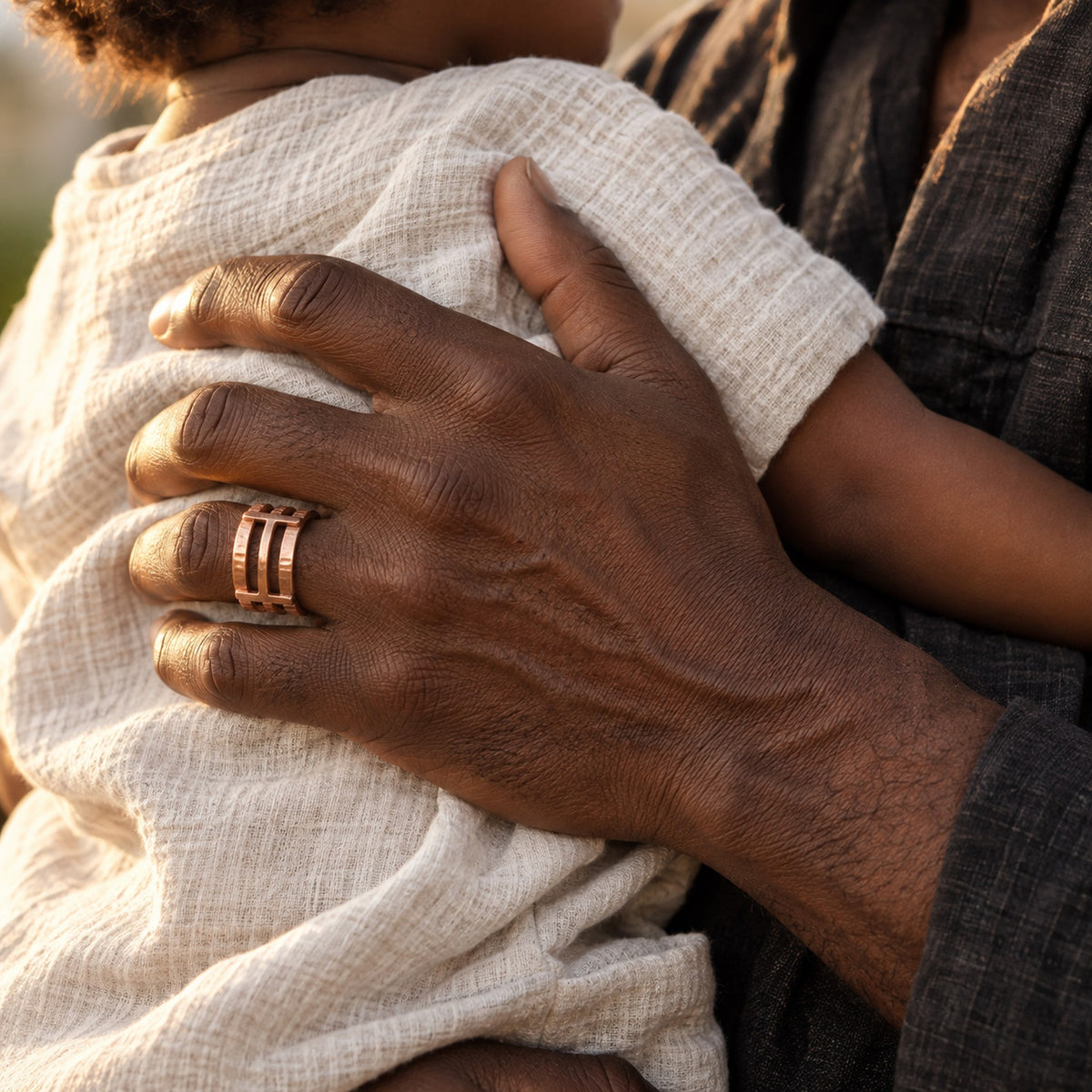 Main d'homme portant la bague Matimba en cuivre, tenant un enfant contre lui