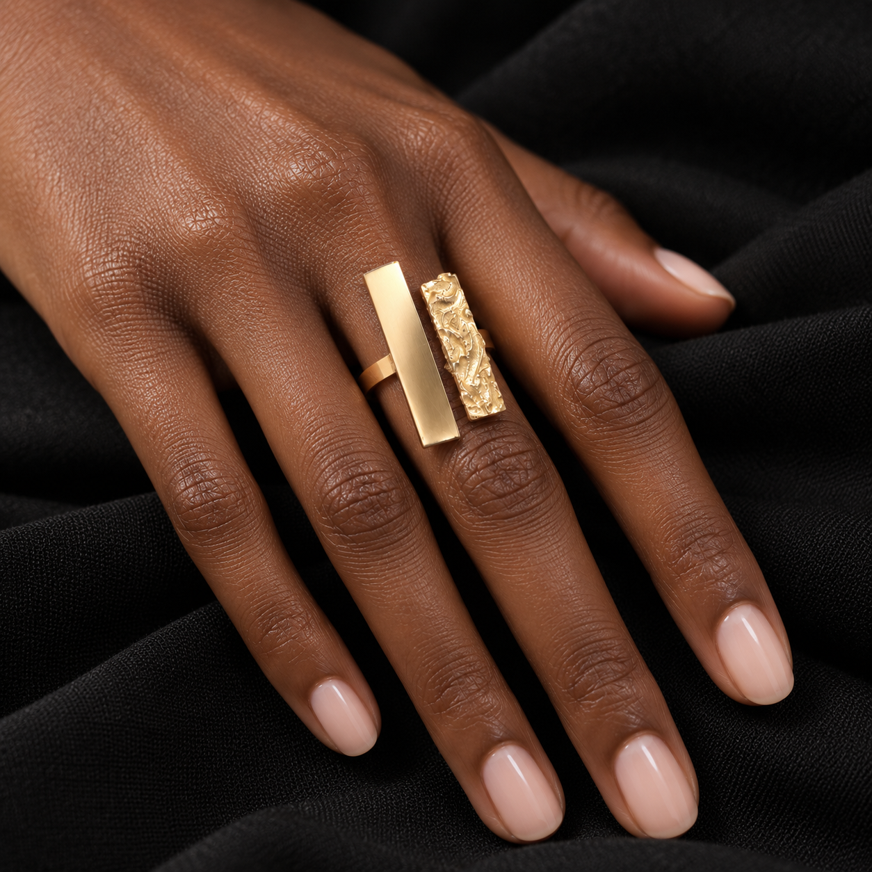 Bague large dorée artisanale africaine portée sur un tissu noir plissé