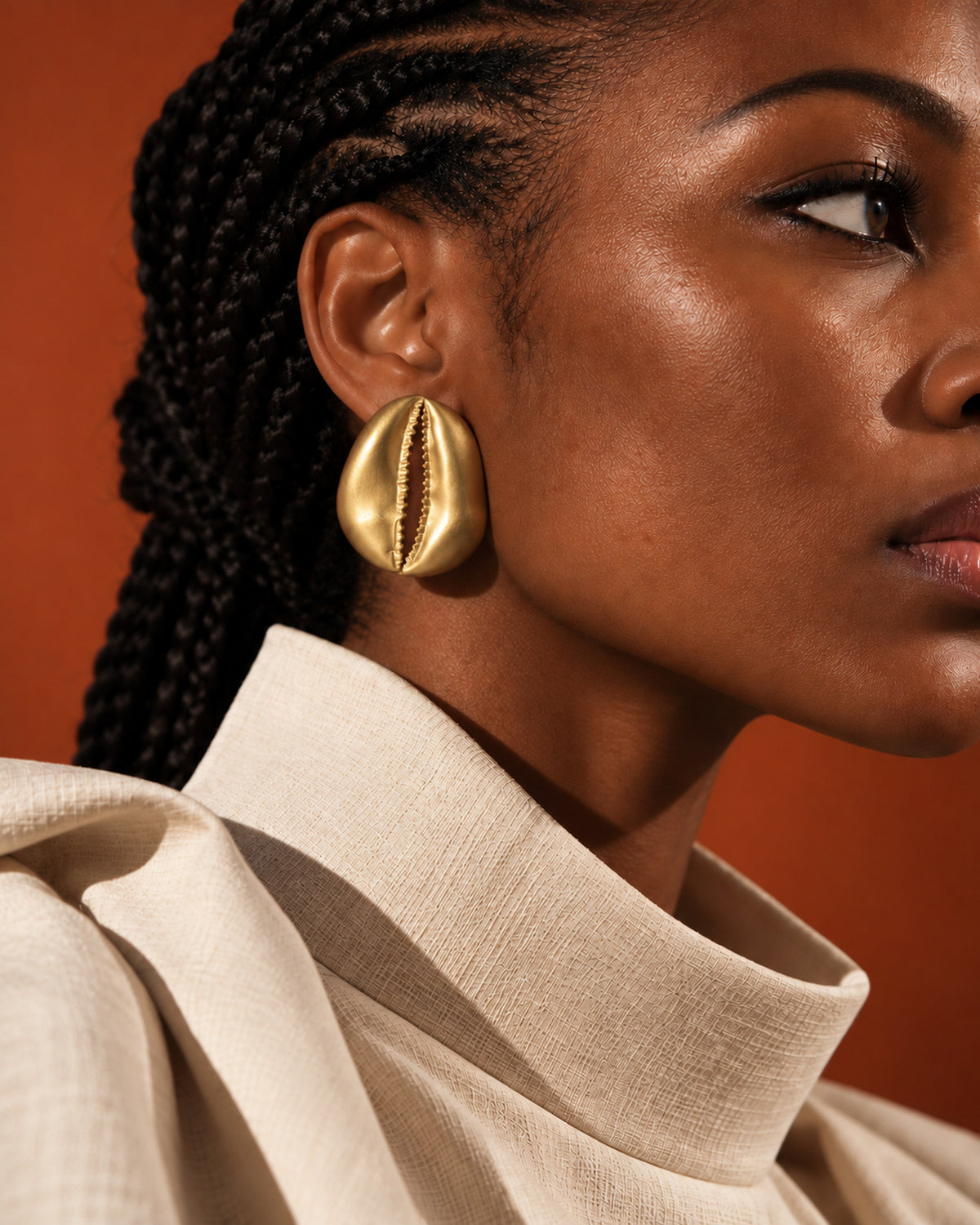 Boucle d'oreille cauri en bronze portée avec un col haut écru sur fond terracotta