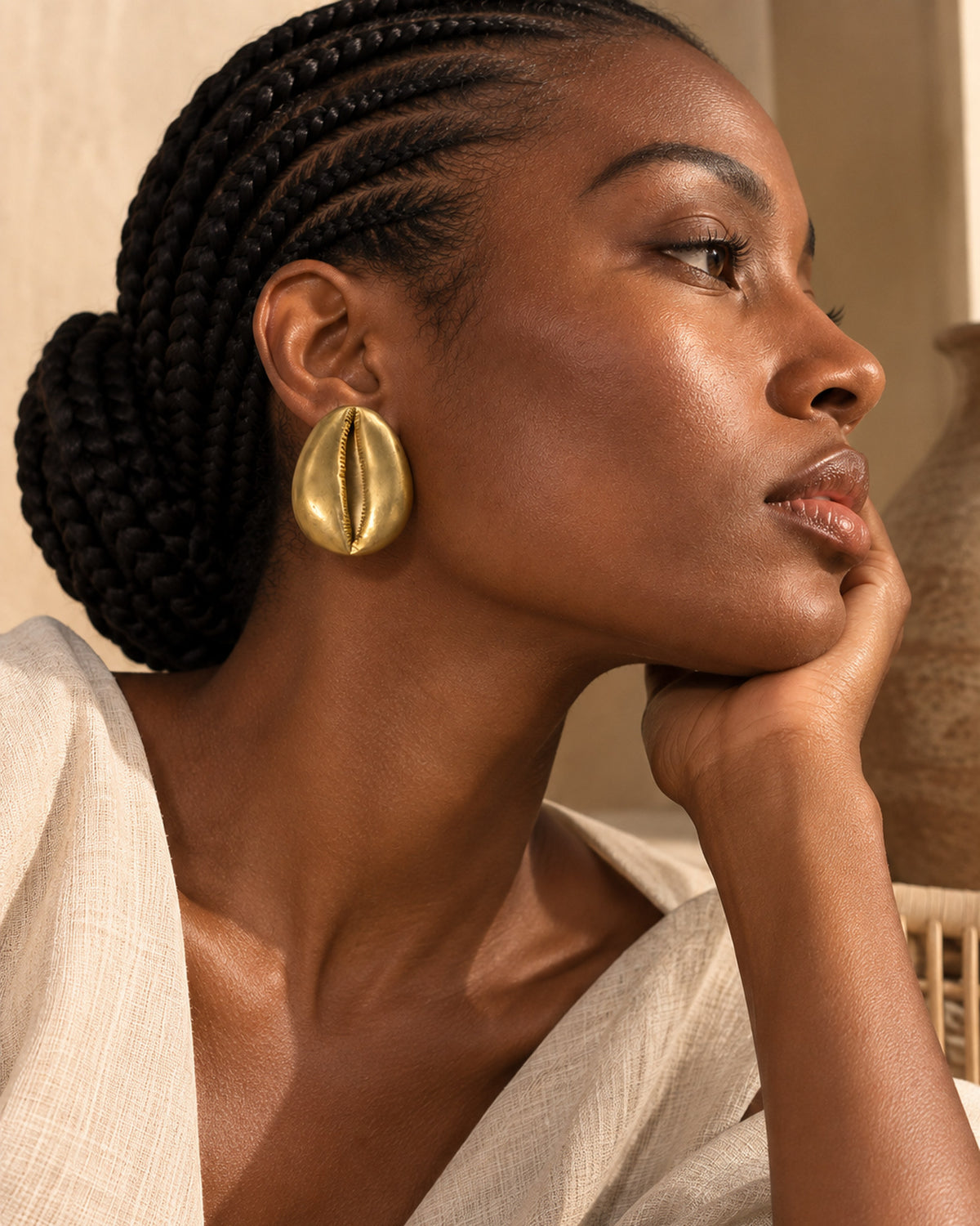 Boucle d'oreille cauri en bronze portée, main au menton et veste en lin écru
