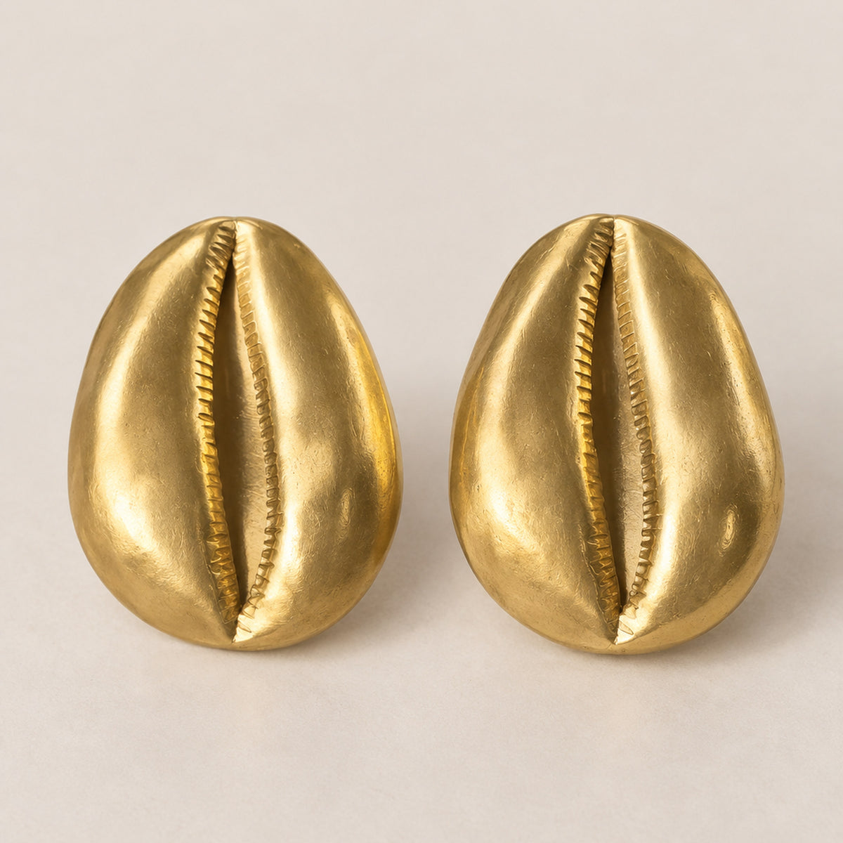 Paire de boucles d'oreilles cauri en bronze doré posées sur fond clair