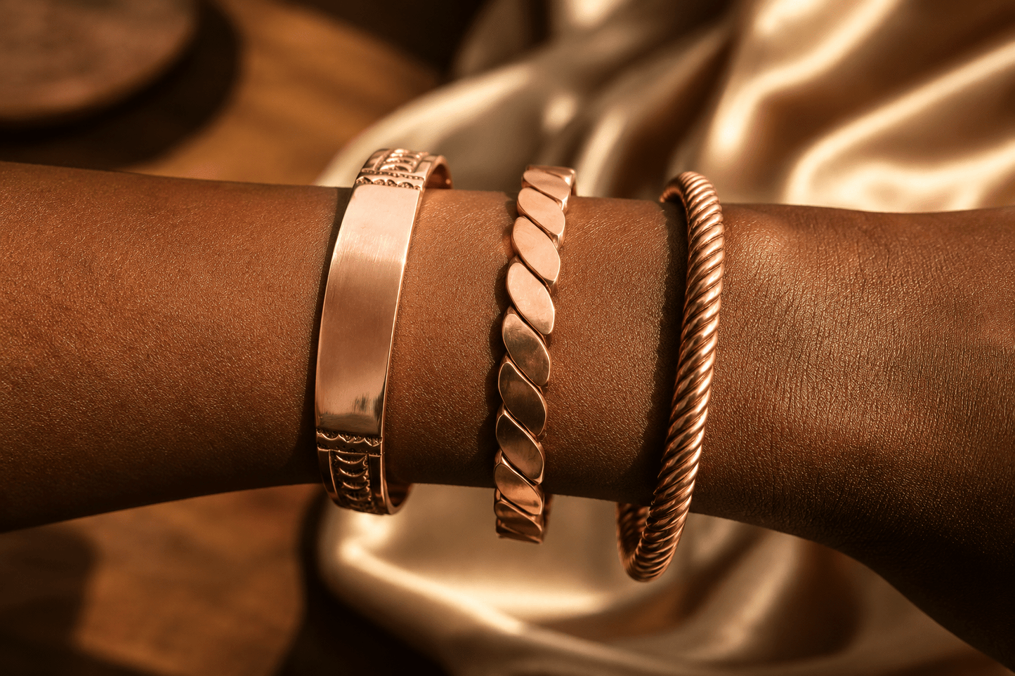 Triptyque Perem : les bracelets en cuivre portés ensemble au poignet, sur une soie dorée