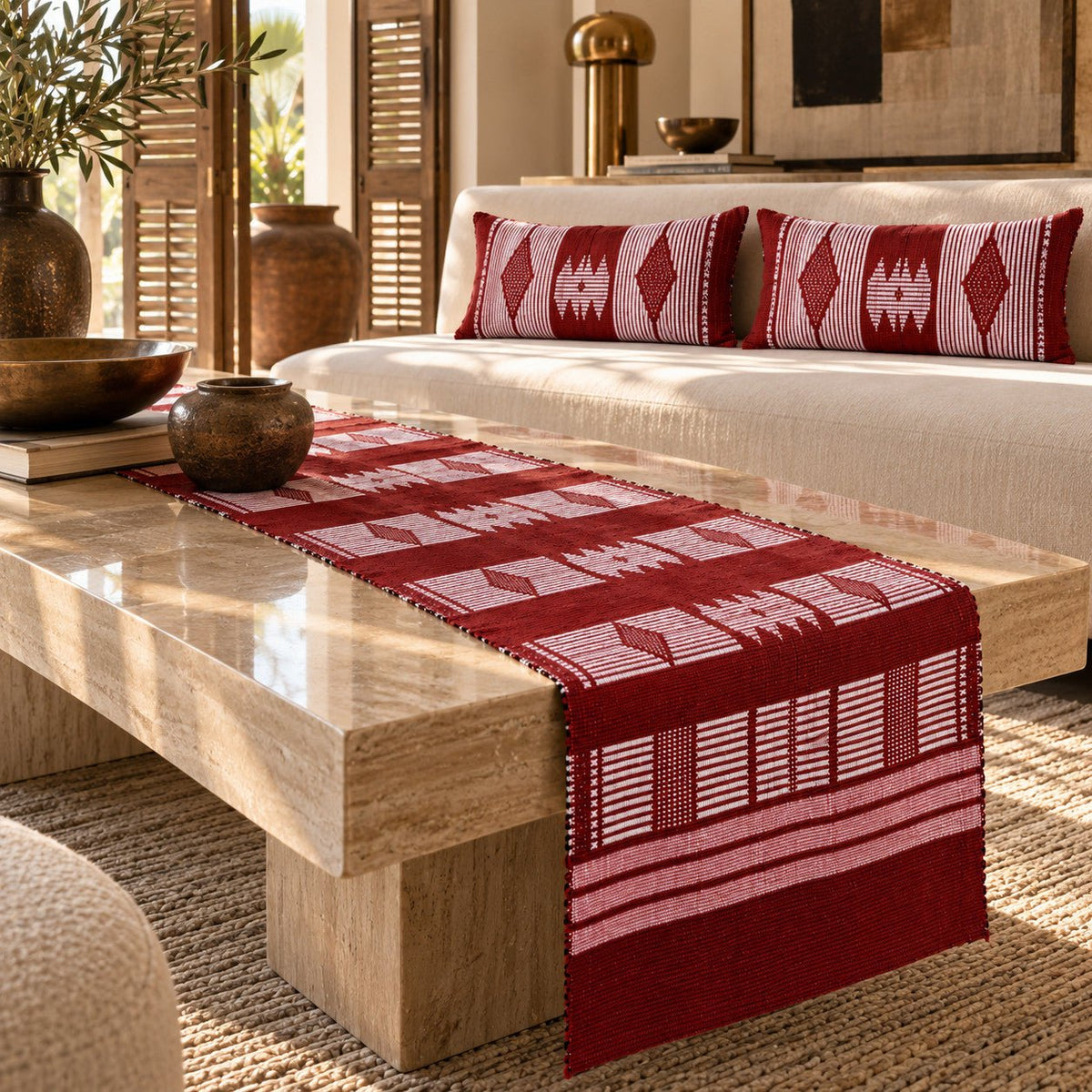 Chemin de table et housses de coussin en pagne Manjak rouge foncé sur une table en travertin