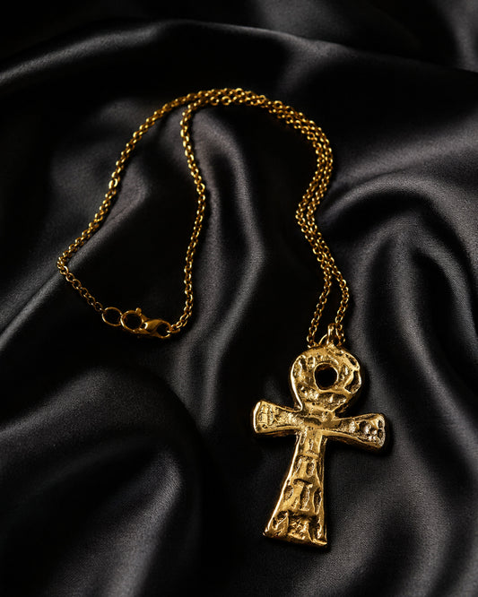 Pendentif croix ankh en bronze martelé sur chaîne dorée, posé sur satin noir
