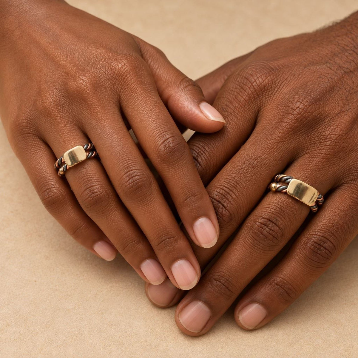 Duo de bagues sénégalaises Ndiaxass : une main de femme et une main d'homme noires portant la même bague à trois métaux
