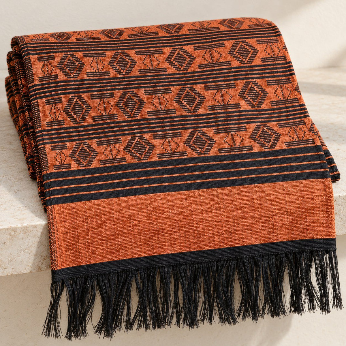 Écharpe-étole Manjak de Luxe orange brique pliée, motifs noirs tissés main sur toute la longueur, bordure orange brique et franges noires
