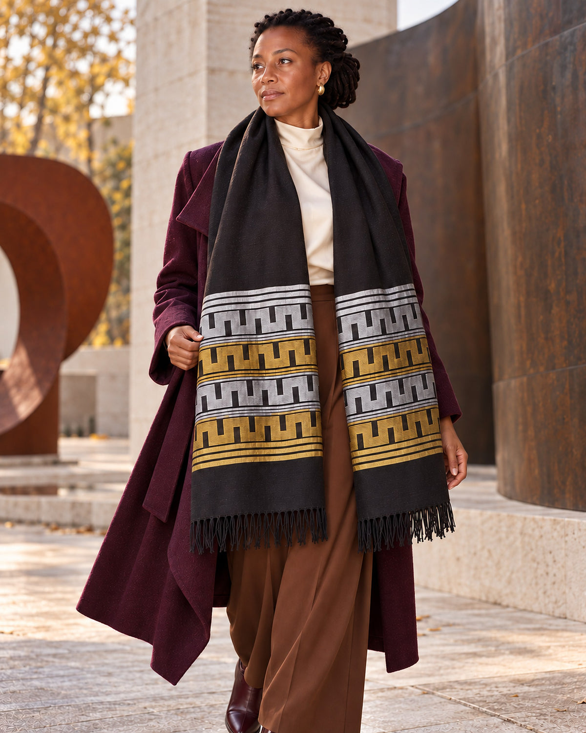 Femme portant l'écharpe Manjak noire, argent et or sur un manteau bordeaux