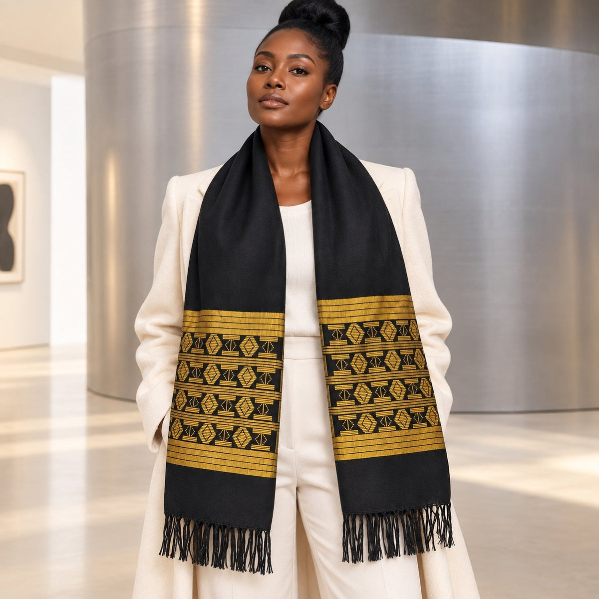 Écharpe Manjak noire et jaune doré, motif 2, portée par une femme sur un manteau blanc