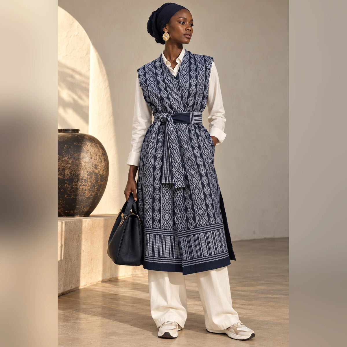 Femme portant le gilet long Manjak bleu marine et gris ceinturé sur une tenue claire