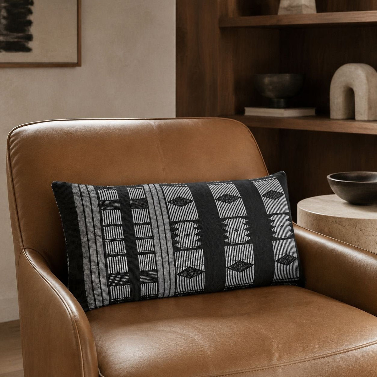 Housse de coussin Manjak noir et blanc sur un fauteuil en cuir fauve