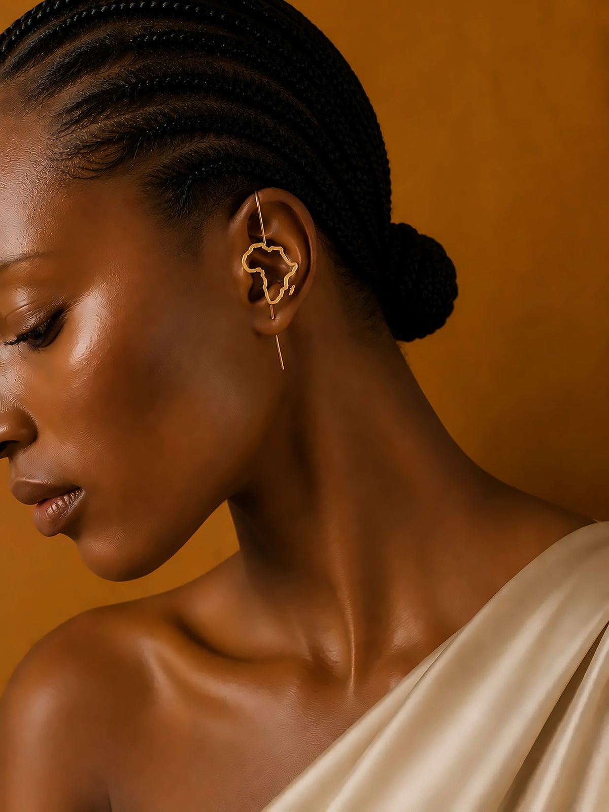 Boucle d'oreille Kemet en bronze doré portée avec un drapé écru sur fond ocre