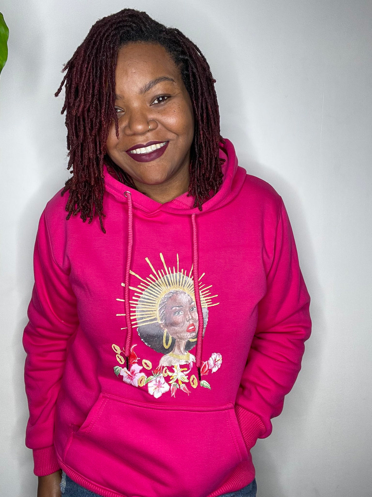 Femme souriante en sweat à capuche rose Grandeur Noire, motif Walatta à l'auréole dorée