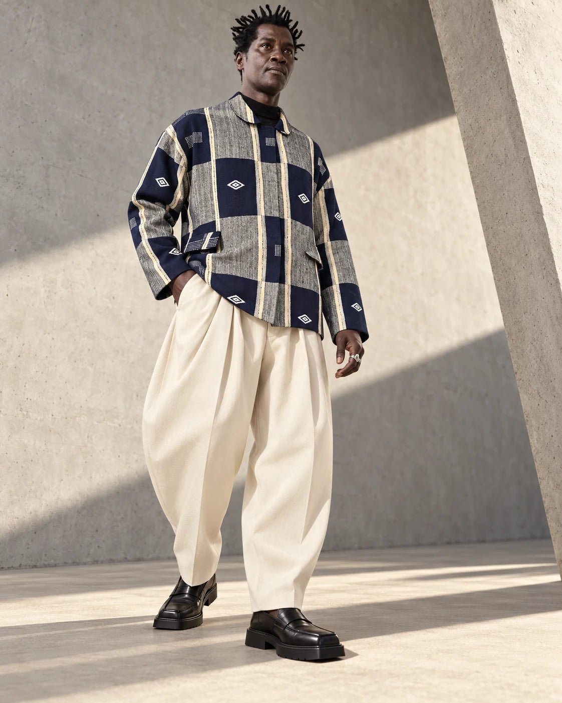 Veste boule Sénoufo fermée portée par un homme avec un pantalon ample écru, vue en pied.