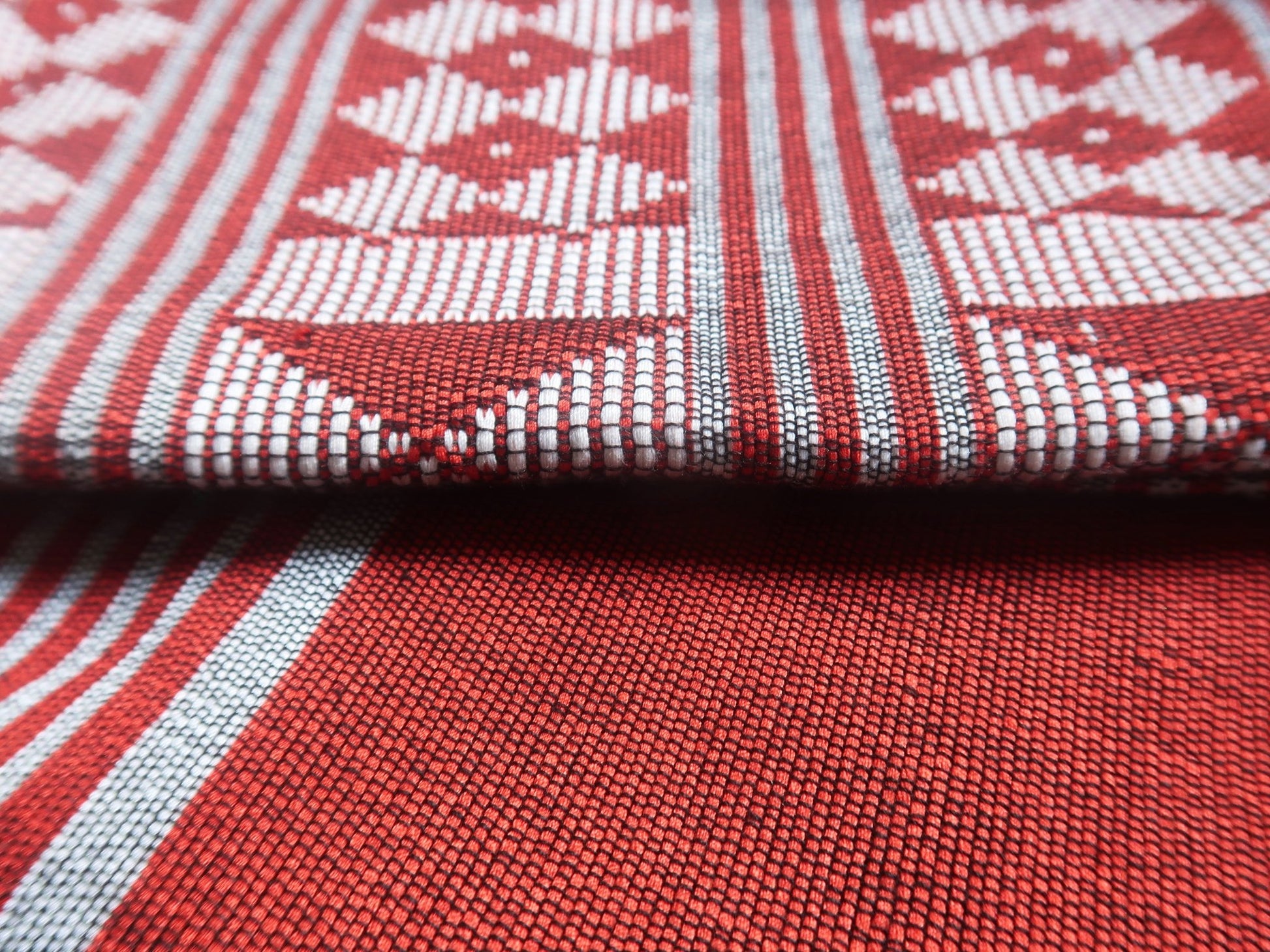 Gros plan sur les motifs géométriques continus du pagne tissé Manjak rouge profond — tissage traditionnel de guinee bissau